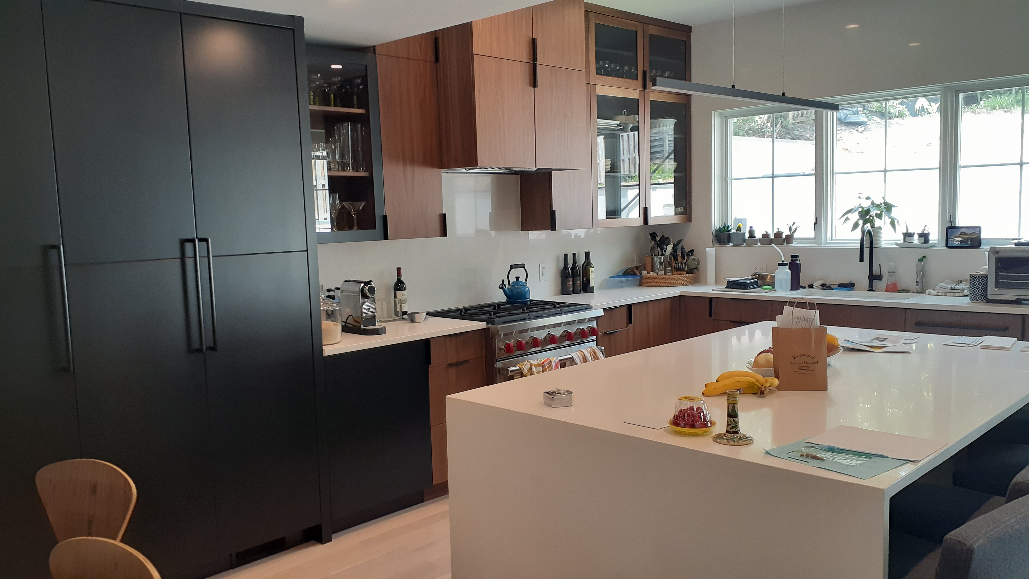 Modern kitchen with matte black tall cabinets, warm wood cabinets with glass doors, white countertops, large island, and black hardware