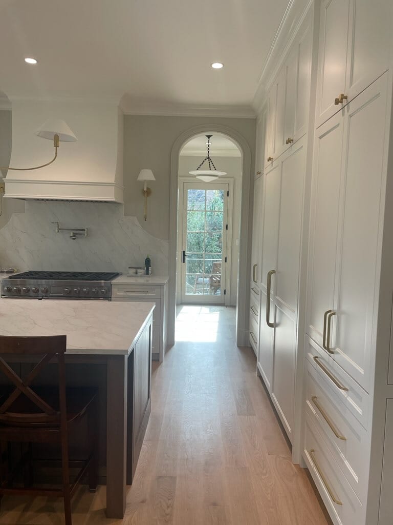 White kitchen cabinetry with a professional range, custom hood, brass hardware, and a dark island