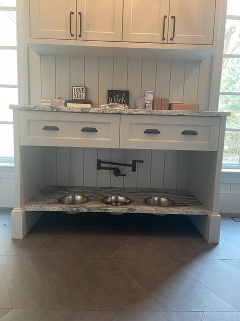 Built-in pet feeding station with three bowls, drawers, upper cabinets, and a wall-mounted faucet