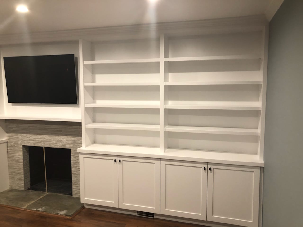 Close view of white built-in shelving and lower cabinets beside a television and fireplace