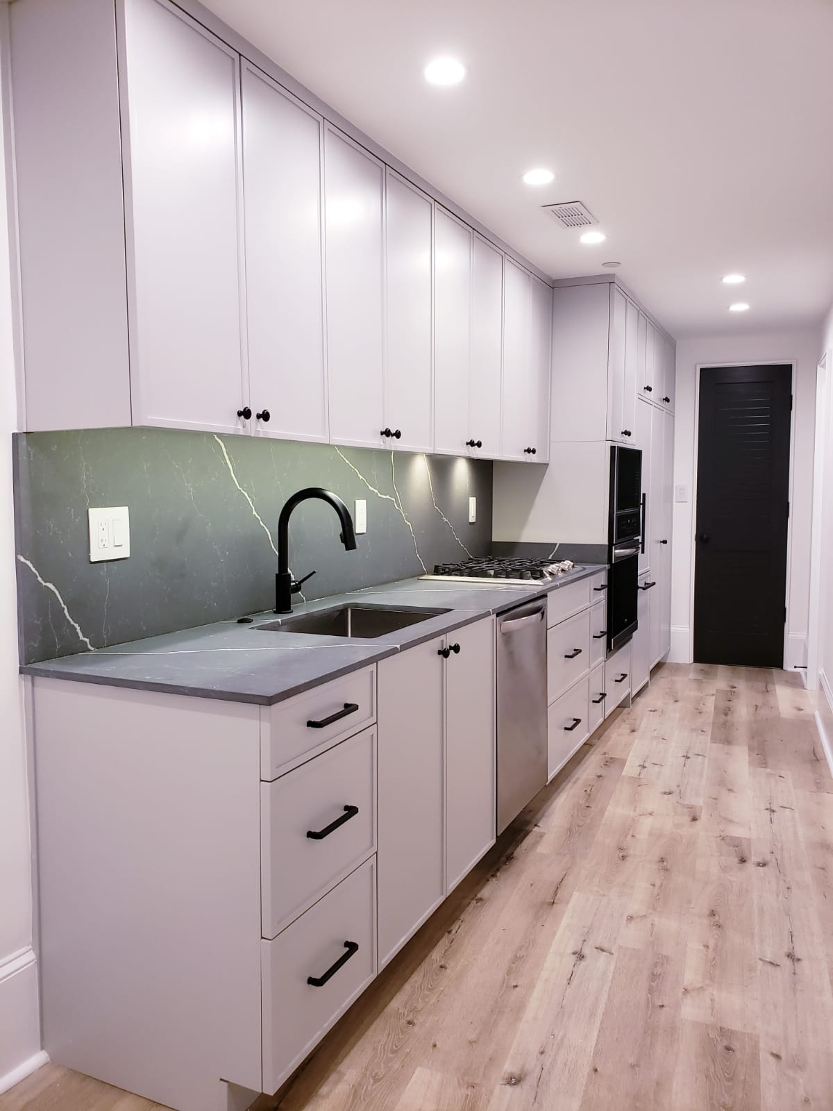 Long galley kitchen with light gray cabinets, black hardware, and a dark veined stone backsplash