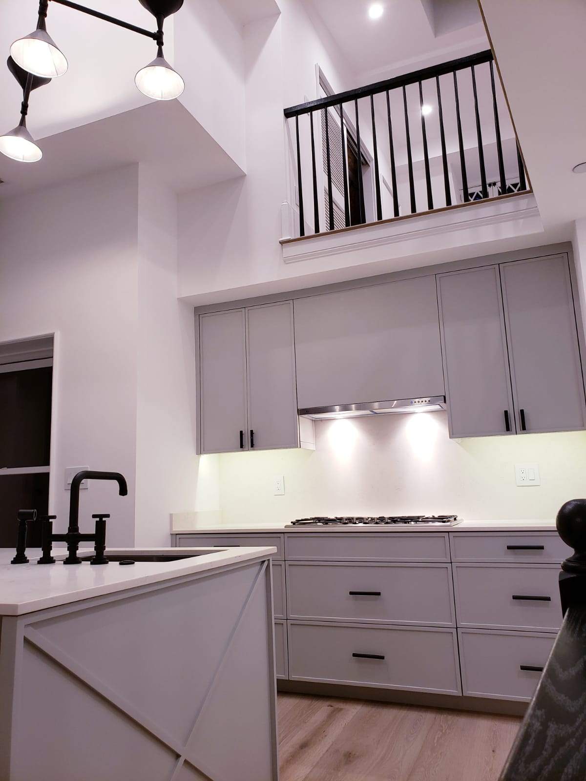 Light gray kitchen beneath an open loft with a white island, black fixtures, and X-panel detailing