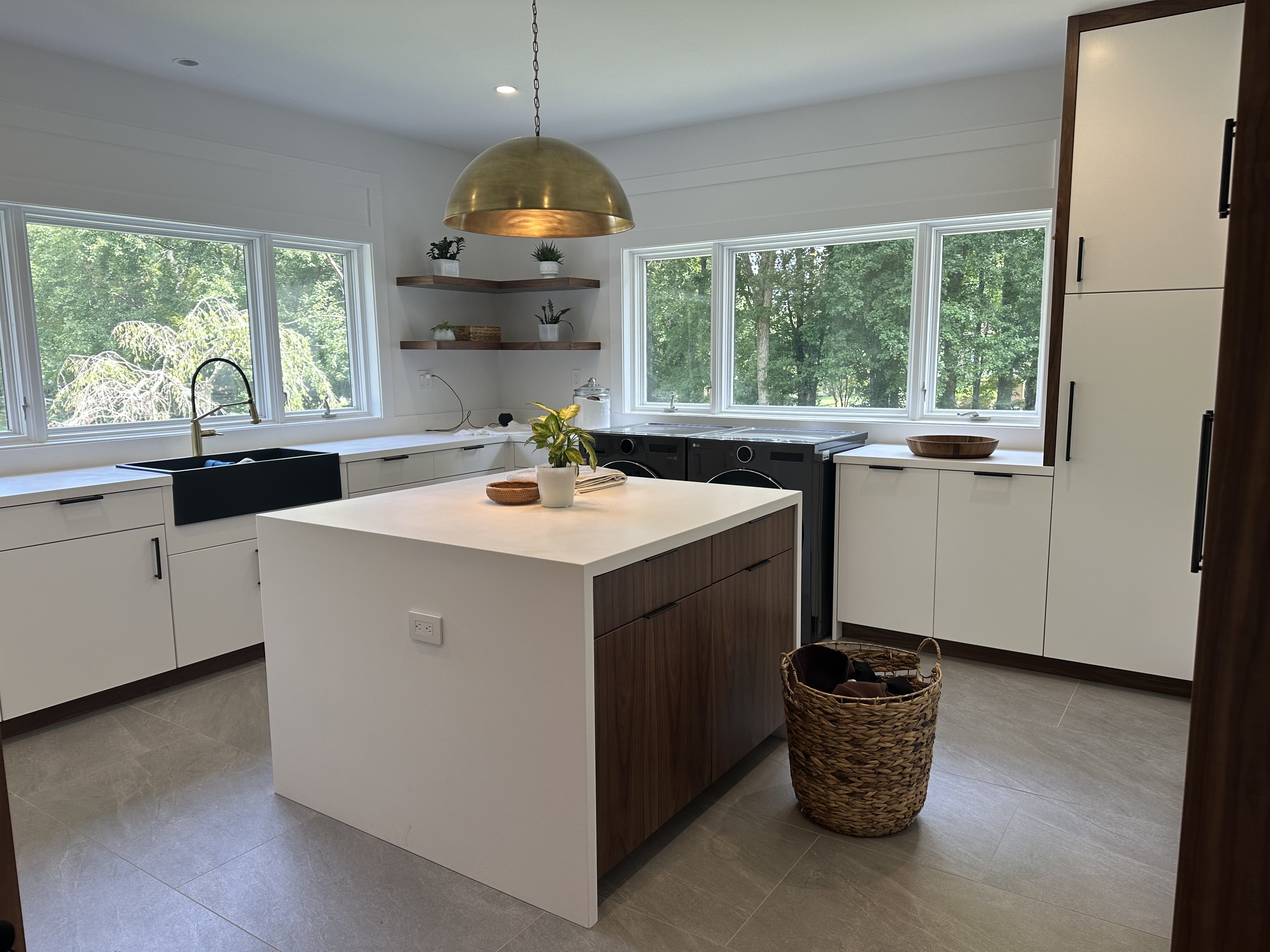 Modern laundry and utility room with white flat-panel cabinets, wood island drawers, black utility sink, tall storage, and laundry appliances