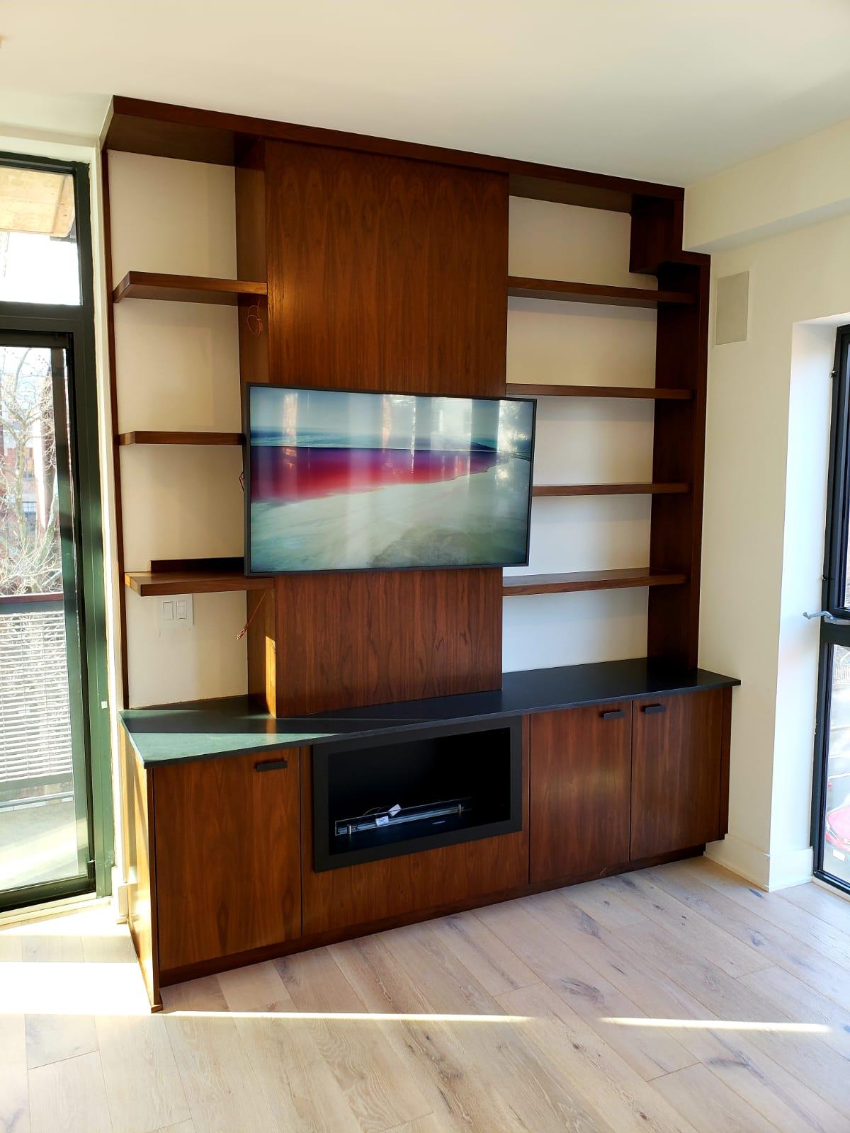 Warm wood built-in media wall with a mounted television, open shelves, black countertop, and lower storage cabinets
