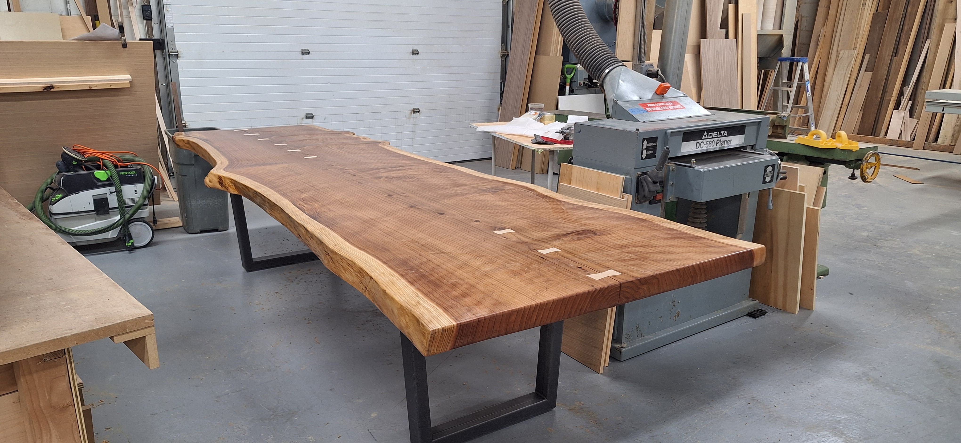 Long live-edge wood slab table with black metal legs in the cabinetry shop