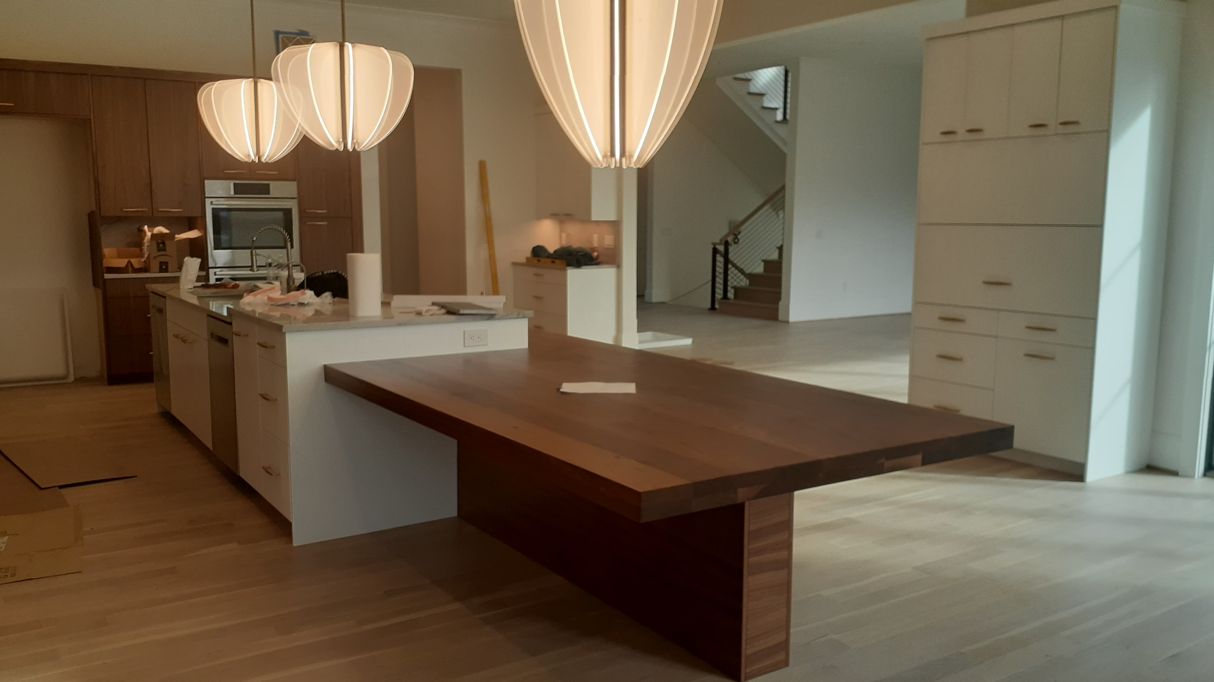 Open kitchen with white island cabinetry, warm wood kitchen cabinets, tall storage wall, and a thick wood dining table attached to the island