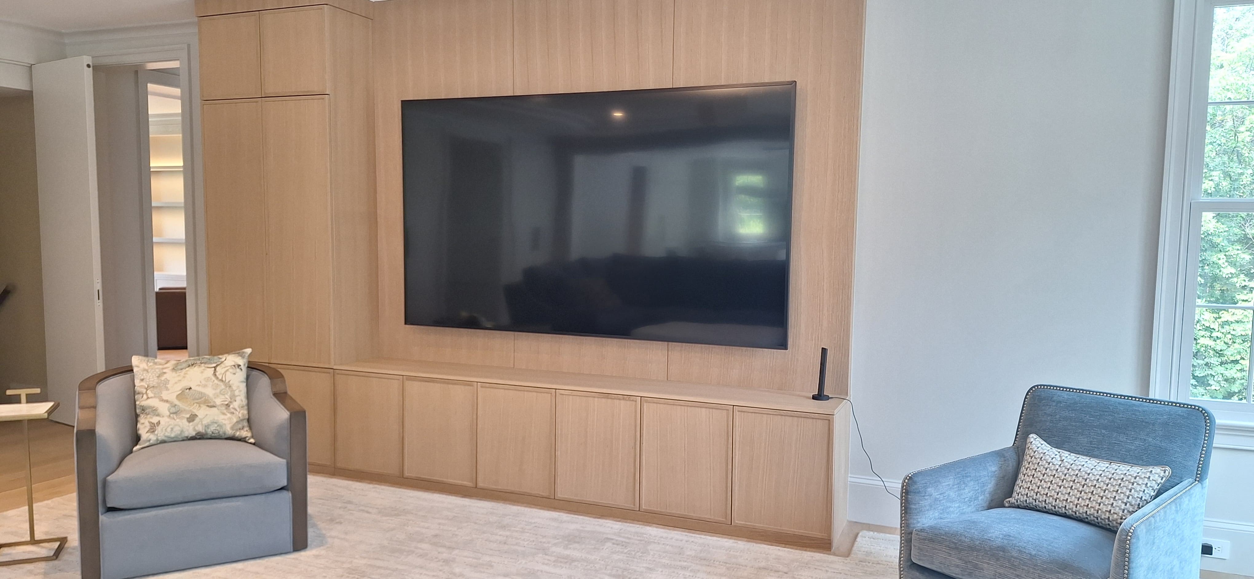 Light wood media wall with a mounted television, floating cabinetry, and a flanking storage column