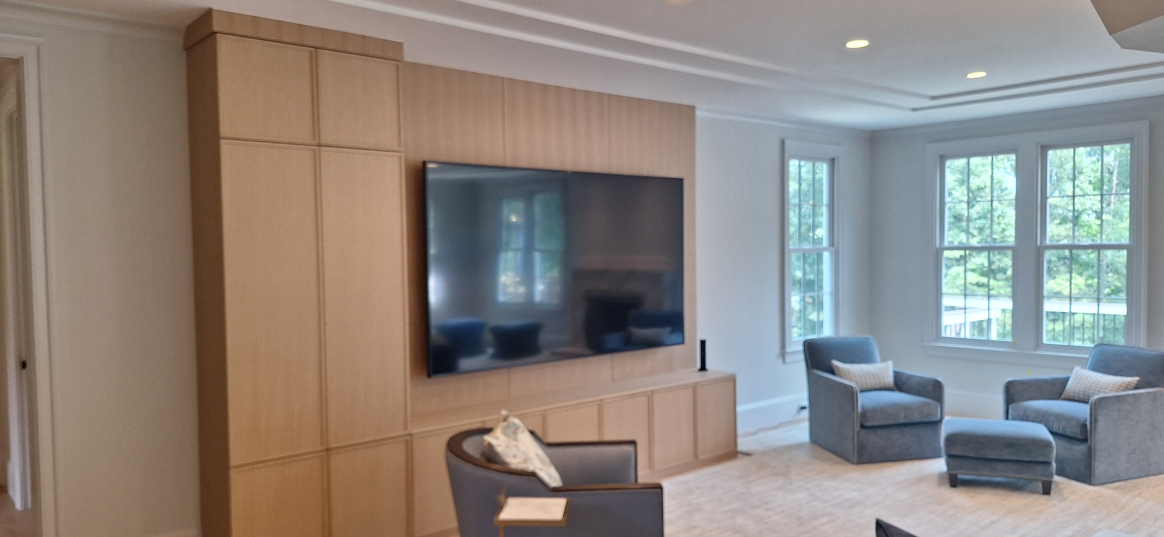 Light wood built-in media wall with a mounted television and tall side cabinet, beside a bay window seating area