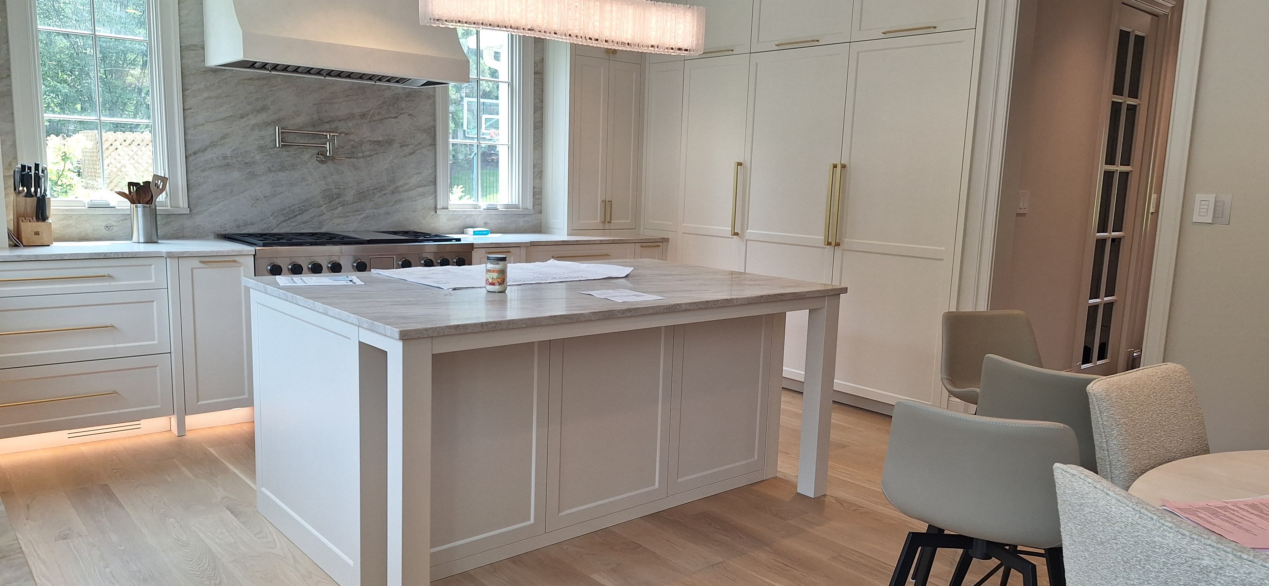 White kitchen island with a marble top and turned furniture-style legs facing a professional range and marble slab backsplash