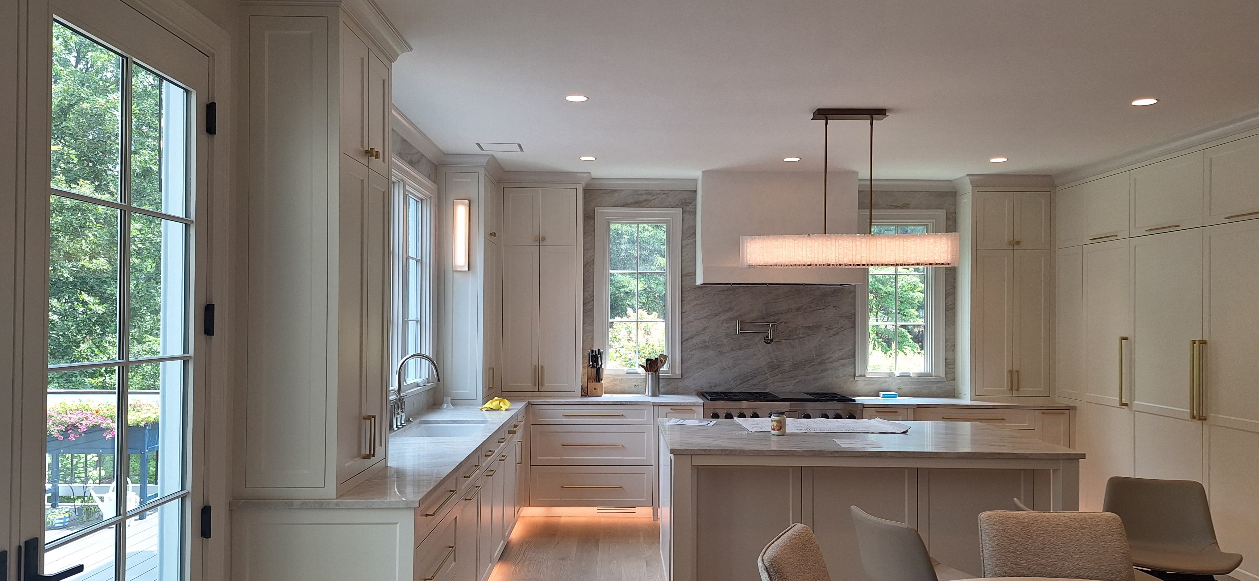 Full U-shaped kitchen with marble slab backsplash, sink wall, French doors, and a linear glass chandelier over the island
