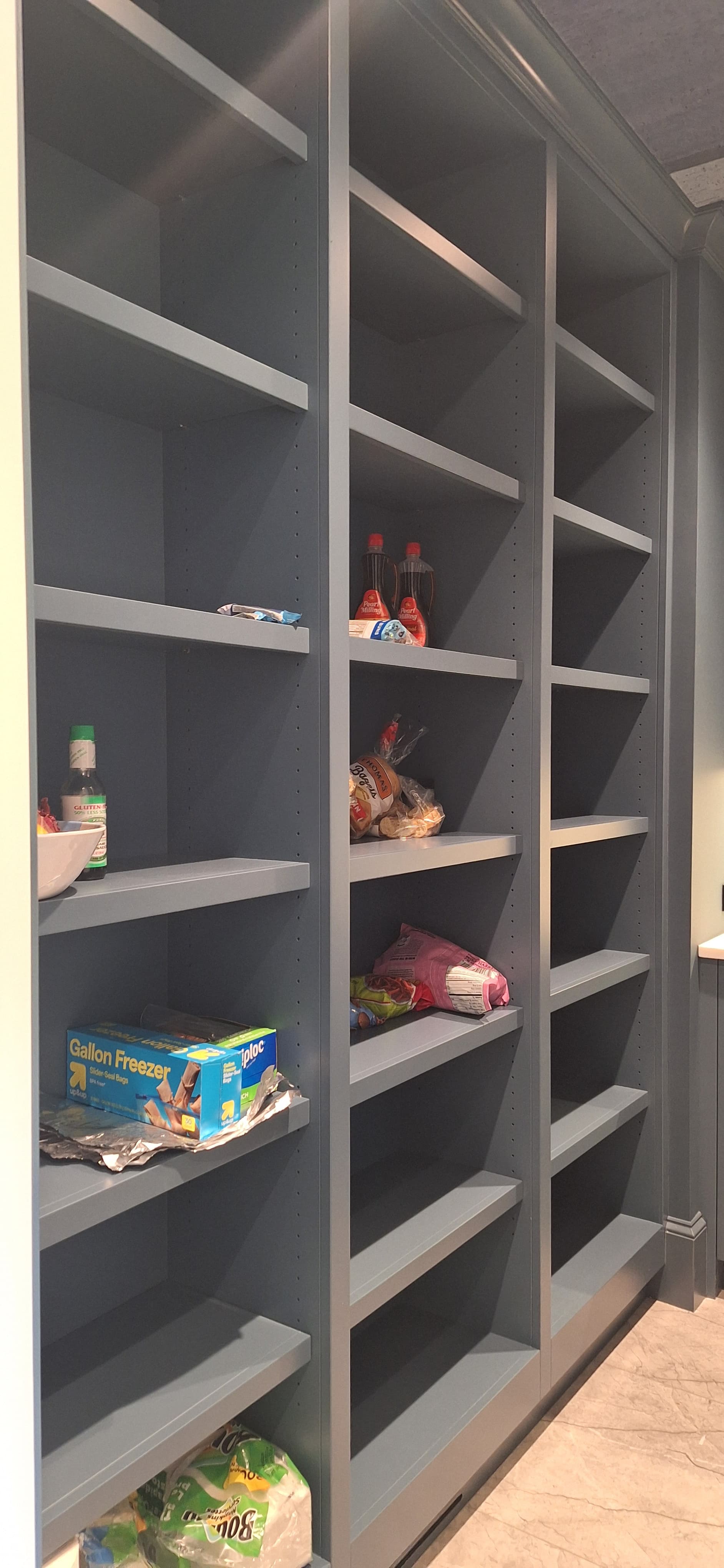 Dark blue-gray walk-in pantry with adjustable open shelving holding pantry staples