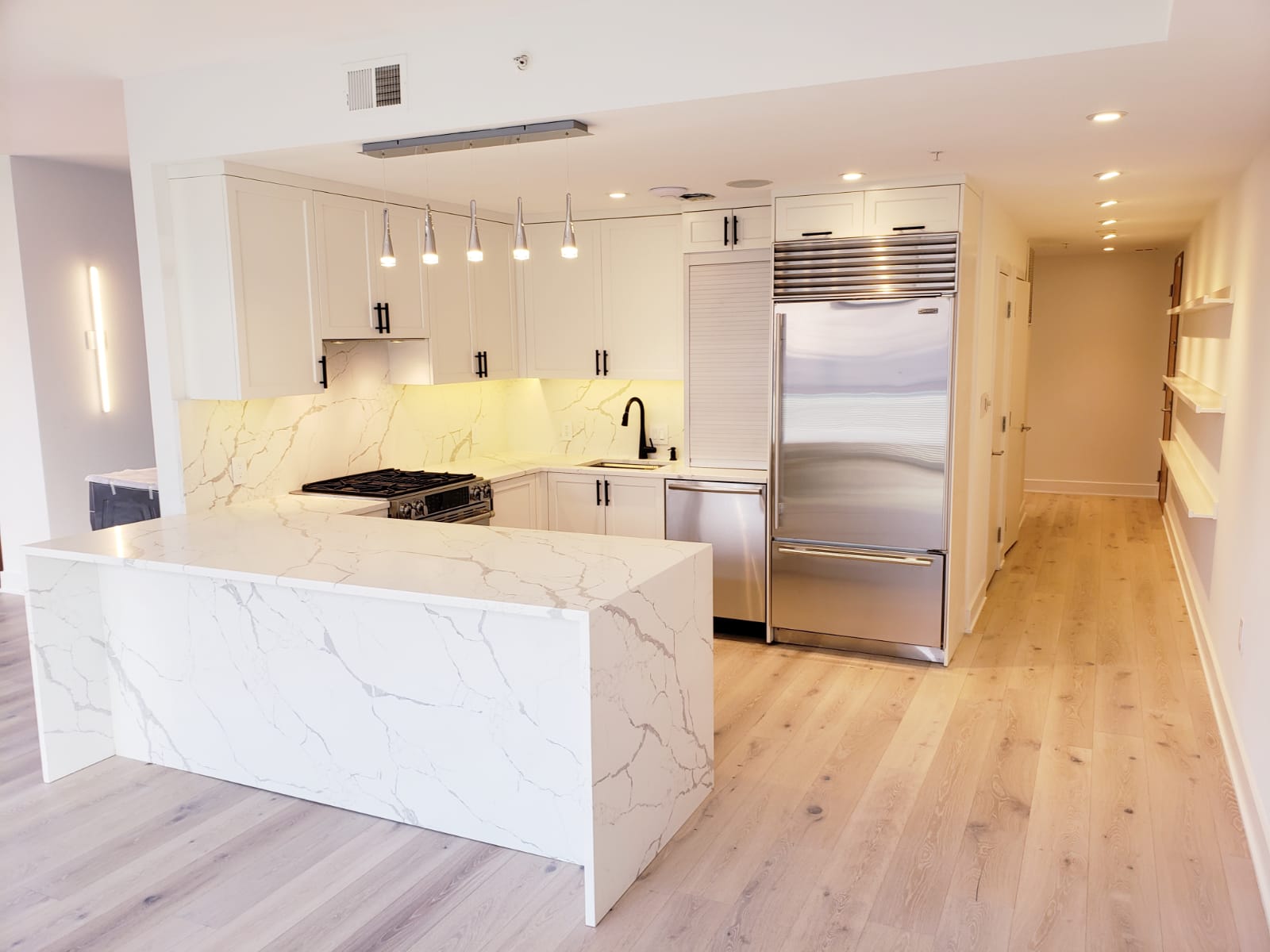 White custom kitchen cabinetry with black hardware, stainless appliances, and a waterfall stone peninsula